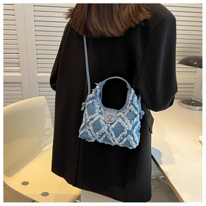 Close-up of light blue denim crossbody bag with quilted frayed edges on black suit model