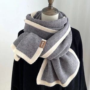 Minimalist dark grey knitted scarf with white trim and leather brand tag on studio background