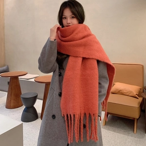 Detail of orange mohair scarf with tassels worn by model in a soft minimalist setting