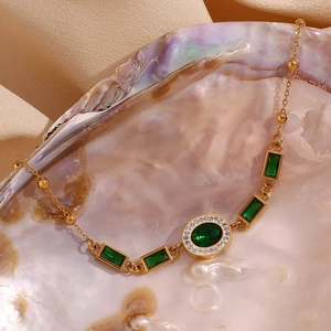 Detail of 18K gold-plated bracelet featuring green emerald-cut stones on silk fabric