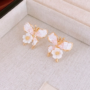 Detailed macro view of golden butterfly earrings with pink crystal and small white flower