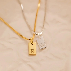 Detailed view of brushed silver and gold rectangular letter pendants with R and W engraving