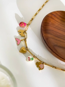 Detail of a gold chain necklace with colorful charms like strawberry, fish tail, and elephant