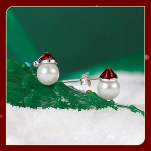 Detail of Christmas pearl earrings with red enamel Santa hat design on snowy tree