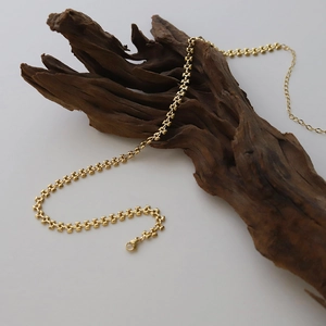 Detailed view of gold wheat link necklace draped over dark wood in minimalist style