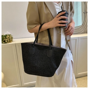 Fashionable black straw tote bag with leather handles shown in a lifestyle model setting
