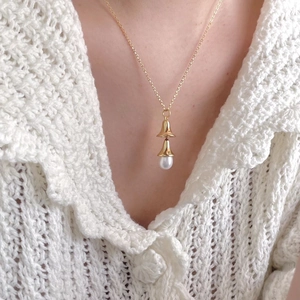 Detailed view of a gold double-bell pendant necklace with a white pearl on a model