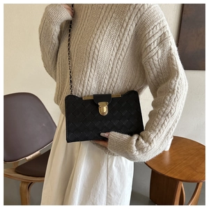 Detail of a black woven leather shoulder bag with a gold chain strap and metal buckle