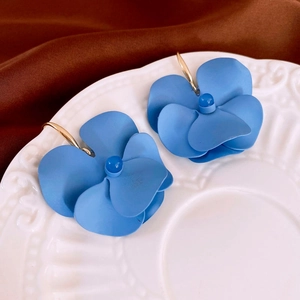 Close-up of blue matte flower petal earrings with gold hooks on a white porcelain plate