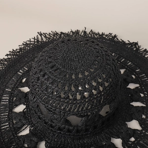 Dettaglio della trama di un cappello da spiaggia in paglia nera intrecciata a mano con frange