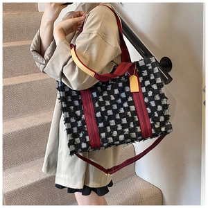 Spacious denim checkerboard tote bag with red strap shown on a model on stairs