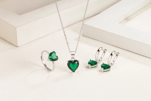 Elegant silver jewelry set with green heart-shaped gemstones on white textured surface