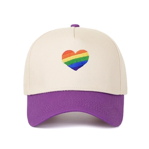 Dettaglio del ricamo a cuore arcobaleno su un cappellino da baseball beige e viola.