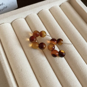 Macro shot of stylish amber leopard print beaded hoop earrings on a beige velvet tray