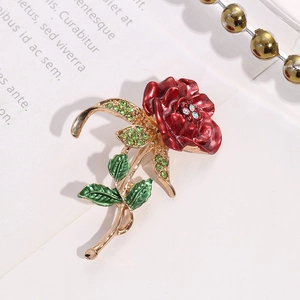 Macro shot of red enamel rose brooch with green rhinestones and golden stem on book