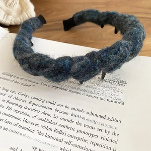 Macro detail of hand-woven mixed blue grey and black acrylic yarn headband on book