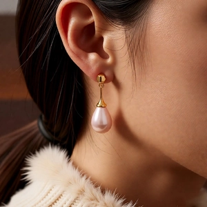 Primo piano di orecchini con perle dorate a goccia su modella per stile vintage