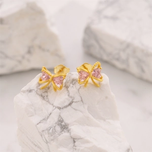 Detail of pink heart zircon earrings with gold bow design on a white marble stone