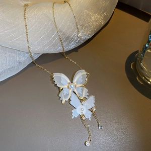 Macro detail of golden necklace with translucent white mesh butterfly pendants and pearls