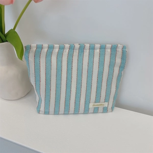 Detail of blue striped canvas bag with zipper closure and woven brand tag on white desk