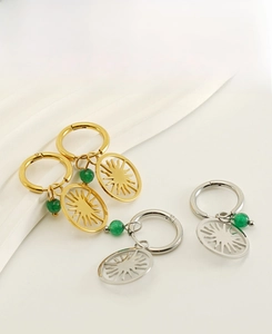Macro view of gold and silver sun hollow earrings with green beads on white fabric