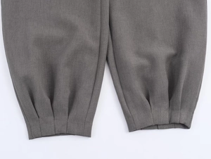 Détail du bas de pantalon gris montrant les coutures et la finition plissée de qualité