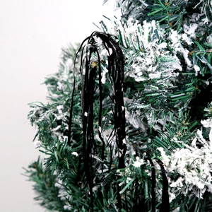 Close-up of black metallic foil tinsel strands hanging on snowy Christmas tree branches
