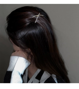 Detail view of a sparkling X-shaped rhinestone hair clip worn on long wavy hair
