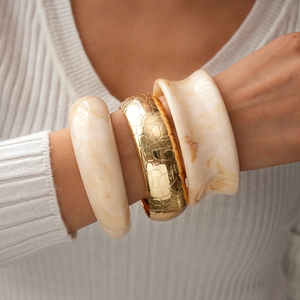 Détail de bracelets en résine marbrée et métal doré texture crocodile sur poignet