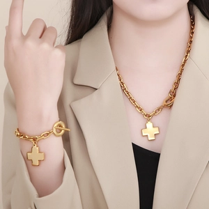 Close-up of golden cross necklace and bracelet set with toggle clasp on model
