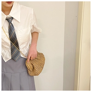 Detail view of a tan woven straw shell bag with a gold metal chain on a school outfit