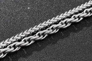Macro detail of silver stainless steel Franco and Figaro chains on a black background