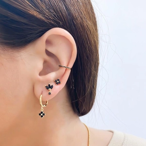 Close-up of gold ear set with black gemstones and clover charms on model's ear