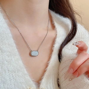 Detail view of a silver oval resin pendant necklace worn on a white knit sweater