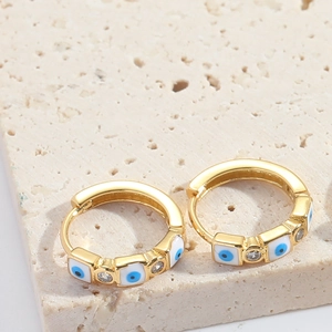 Detail of gold evil eye hoop earrings with white zircon on beige stone background