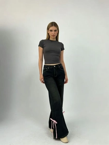 Dettaglio di fiocchi in rosa sul lato dei jeans neri a vita alta e gamba larga