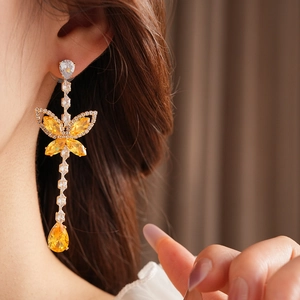 Close-up of elegant long butterfly drop earrings with yellow faceted stones and gold setting
