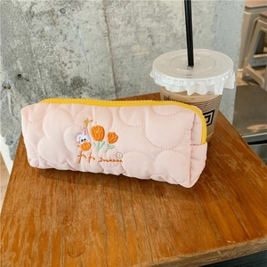 Close-up of pink quilted pencil case with rabbit embroidery and yellow zipper on a wood table