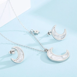 Detail of silver star and moon jewelry set with white mother of pearl inlay on blue surface