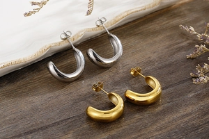 Detailed view of polished gold and silver C-shape earrings on a textured wooden table