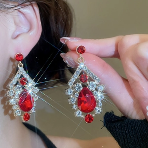 Close-up of luxury gold-plated drop earrings featuring large red rhinestones and crystals