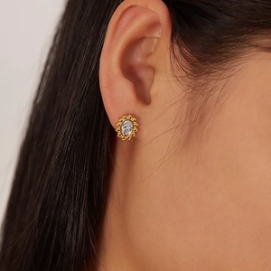 Detail of gold sunflower stud earring with an oval zircon stone worn by a model