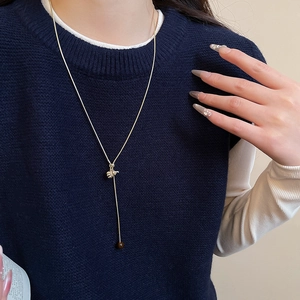 Golden Y-shaped necklace with floral pendant on blue sweater background