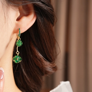 Detailed close-up of gold vintage drop earrings with green rhinestones on model