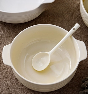 Detail of cream ceramic soup bowl with handles and matching spoon on brown linen cloth