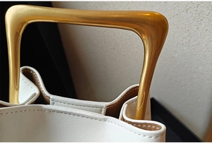 Detail shot of a white bucket bag featuring a unique gold metal handle and PU leather texture
