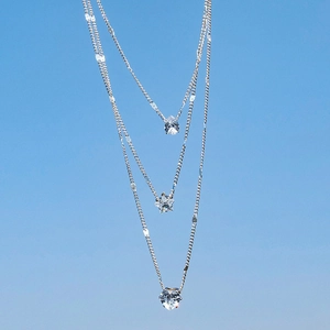 Three-layer silver necklace with teardrop, star and heart crystal charms against a blue sky