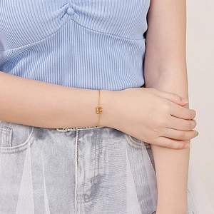 Elegant gold-tone link bracelet featuring a diamond-set letter E charm on woman's wrist