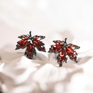 Nahaufnahme eleganter Ahornblatt-Ohrstecker im Vintage-Stil mit roten Kristallsteinen