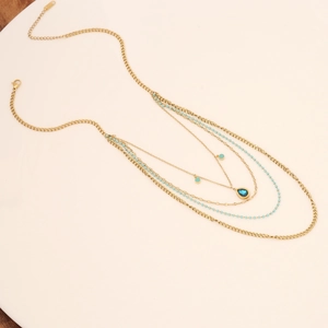 Multi-layer gold necklace with blue beads and a teardrop pendant on a white tray